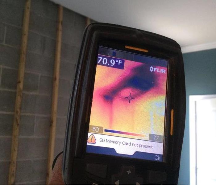 Thermal camera in action pointed towards a ceiling showing a dark spot where water is hidden. 